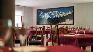 Un comedor con mesas dispuestas para comer, sillas y un cuadro grande enmarcado con un paisaje de montaña en la pared.