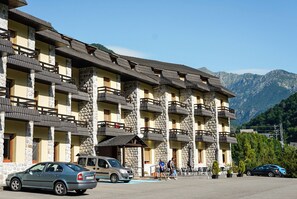A multi-story hotel with stone pillars and balconies, a parking area, and a mountainous backdrop. - Snö Bielsa (Bielsa)