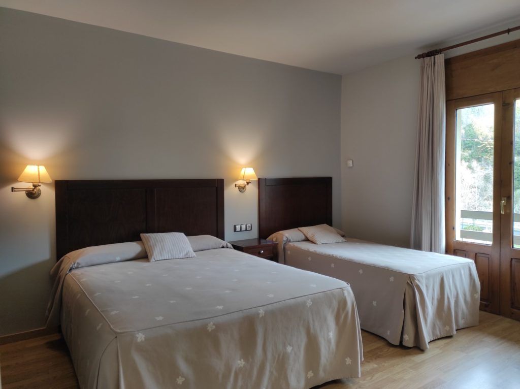 Una habitación de hotel con dos camas, cada una con cabecera y lámparas de noche.