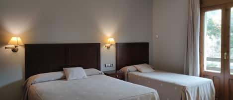 A hotel room with two beds, each with a headboard and bedside lamps.