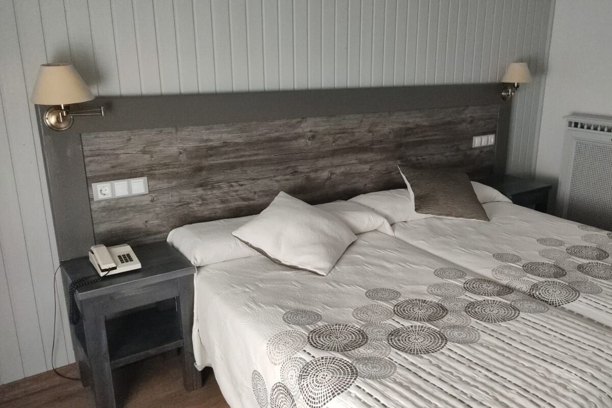 A bedroom with a wooden headboard, a bed with a patterned bedspread, two bedside lamps, and a nightstand with a telephone.