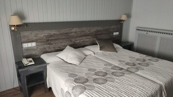 A bedroom with a wooden headboard, a bed with a patterned bedspread, two bedside lamps, and a nightstand with a telephone.