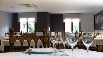 Un comedor con mesas dispuestas para una comida, con sillas de madera y vasos transparentes.