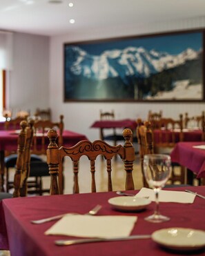 A dining area with tables set for two, wooden chairs, and a large mountain painting on the wall. - Snö Bielsa (Bielsa)