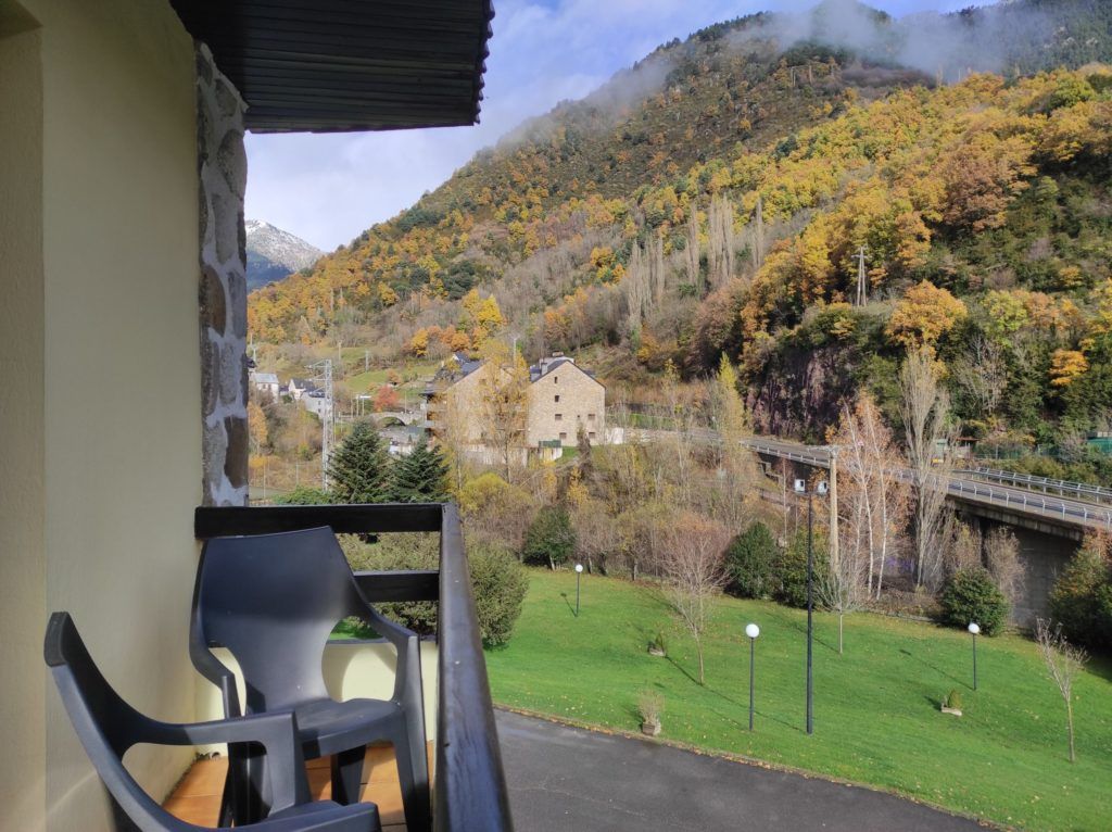 Un balcón con vistas a un paisaje montañoso, un muro de piedra y una silla.