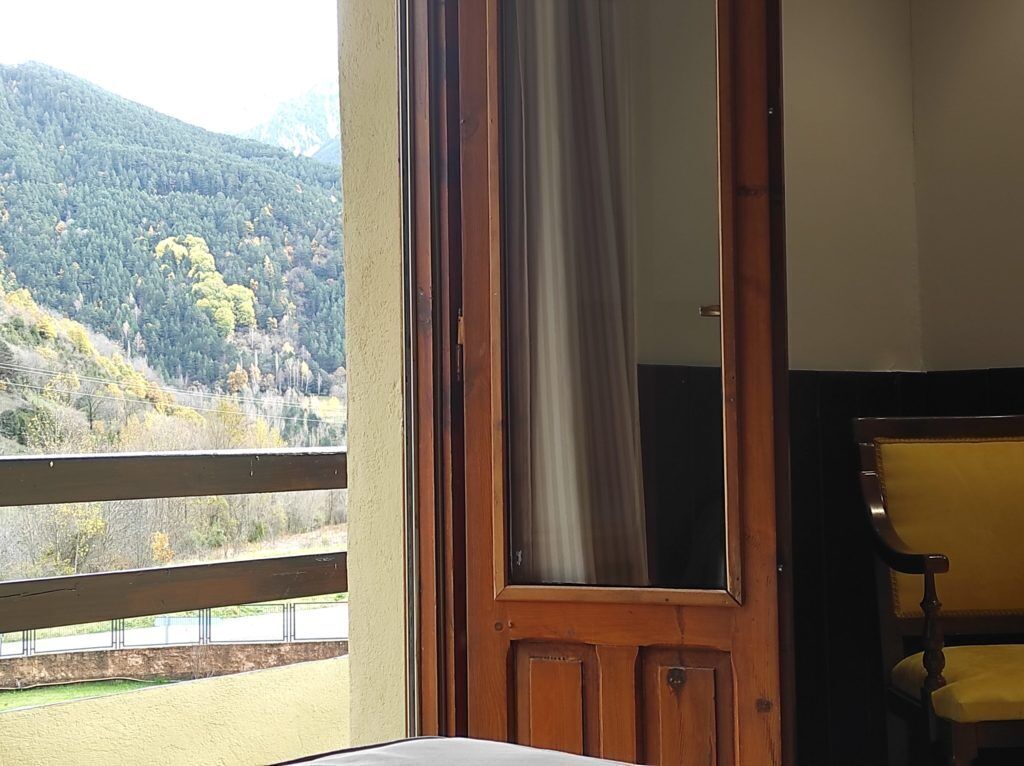 Une pièce avec une porte en bois, une chaise jaune et une vue sur une colline boisée.