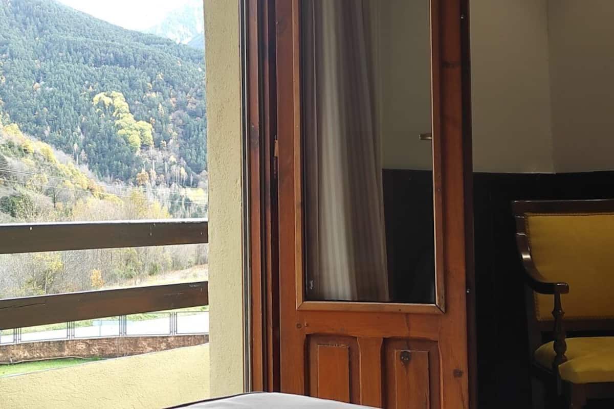 A room with a wooden door, a yellow chair, and a view of a forested hillside.