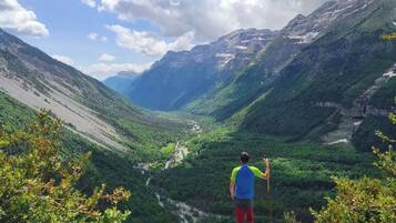 Una persona de pie sobre un afloramiento rocoso, con vistas a un valle y un río, rodeado de montañas.