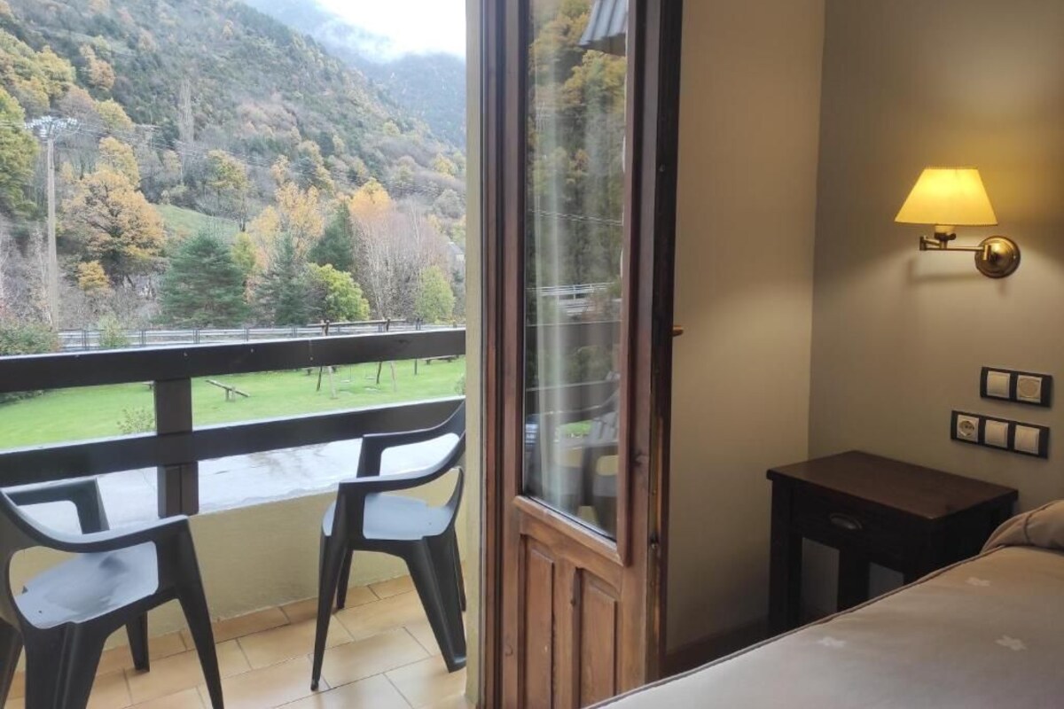 A balcony with a view of a forested hillside, a small table, and a chair.