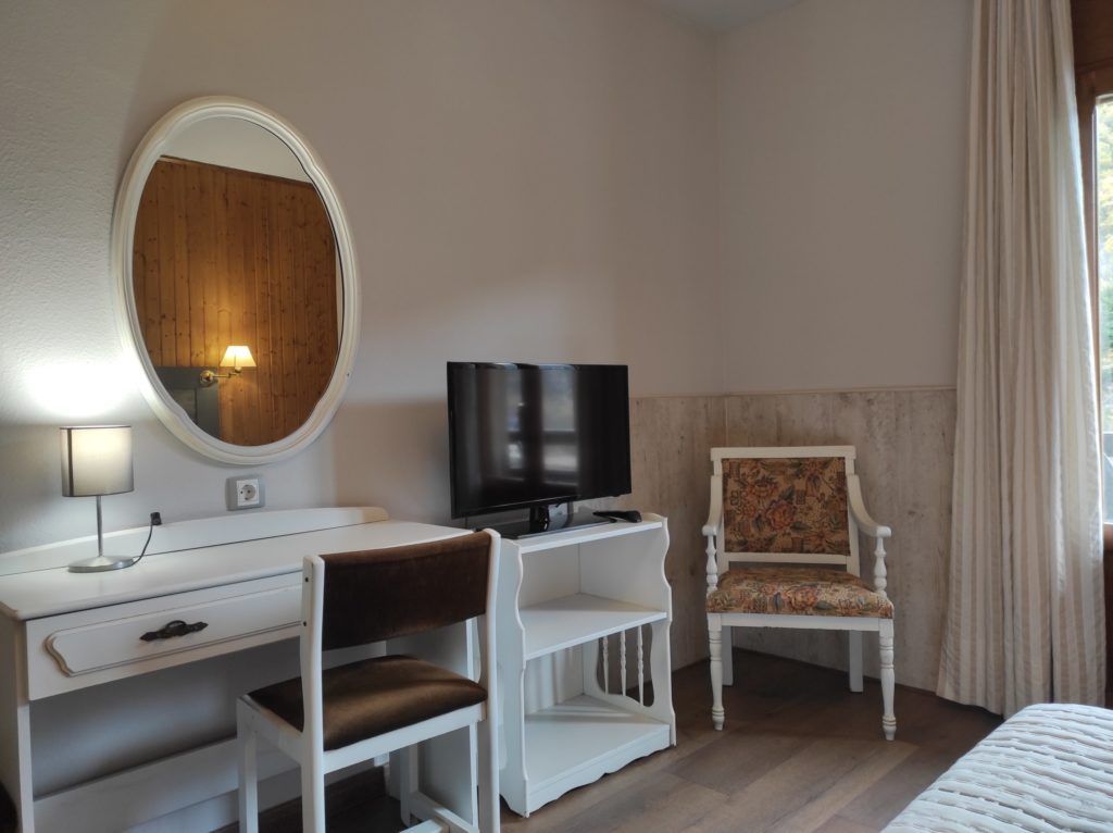 Una habitación de hotel con un escritorio blanco, televisión, una silla y una cama.