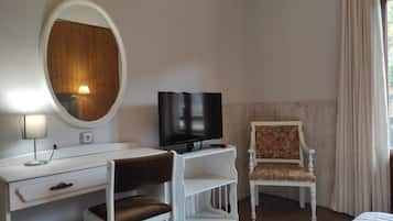 Una habitación de hotel con un escritorio blanco, televisión, una silla y una cama.