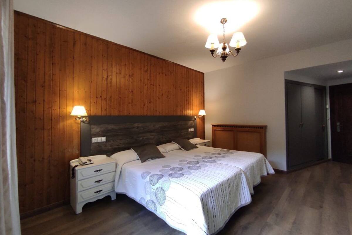 A bedroom with a wooden wall, a bed with a patterned bedspread, bedside lamps, and a chandelier.