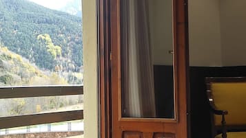 Una habitación con una puerta de madera, una silla amarilla y vistas a una ladera boscosa.