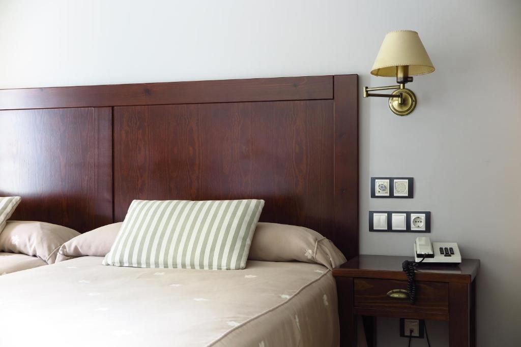 A hotel room with a wooden headboard, a bed with beige bedding, a bedside table with a lamp, and framed pictures on the wall.
