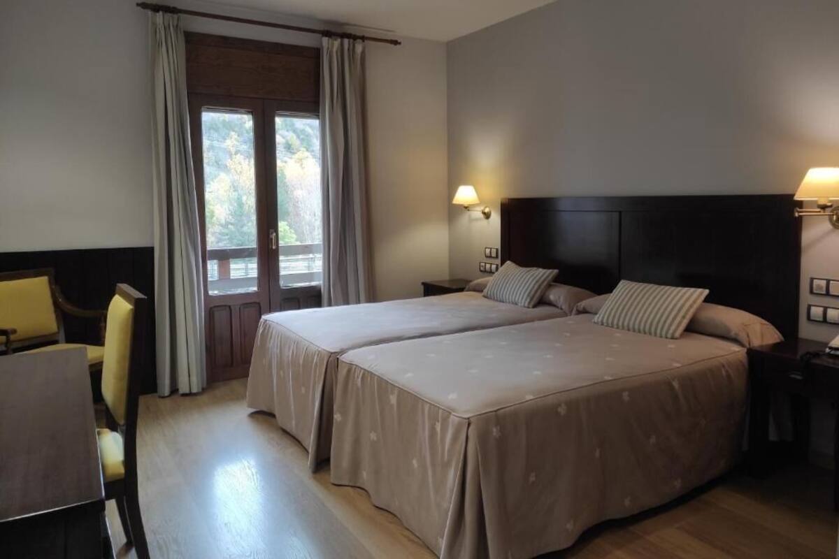 A hotel room with two beds, a desk, and a chair.