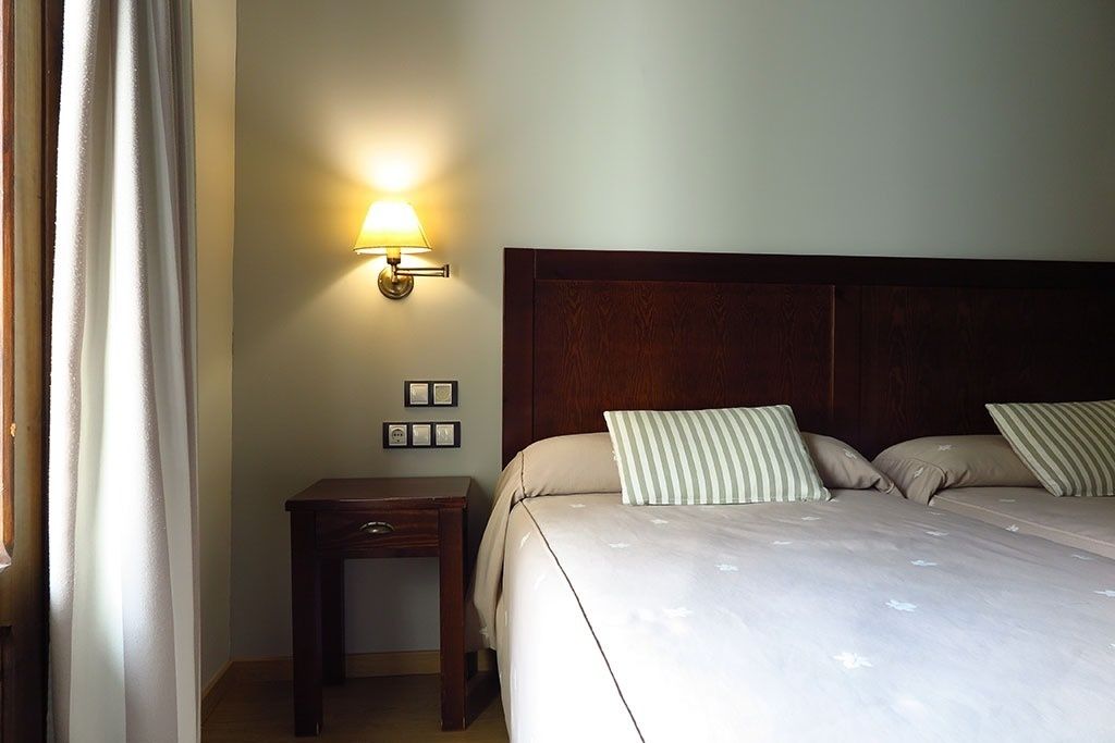 A hotel room with a bed, bedside table, lamp, and wall-mounted light.
