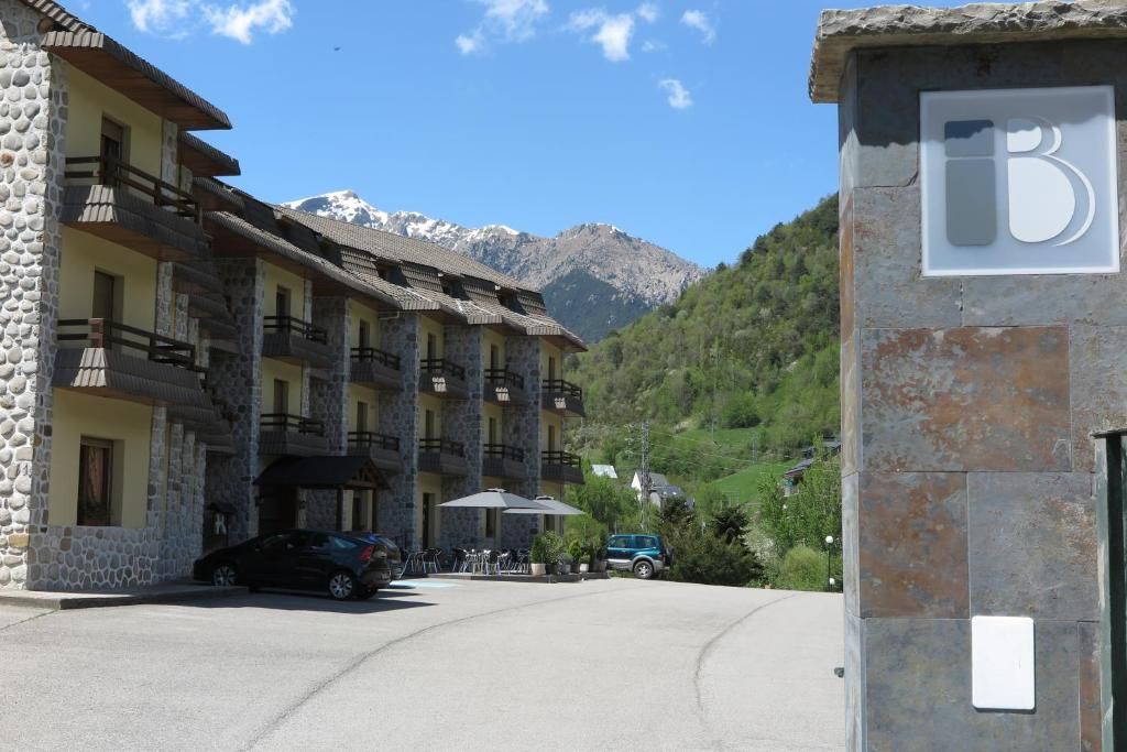 Un hotel de fachada de piedra, con varios balcones y el paisaje de una montaña al fondo.