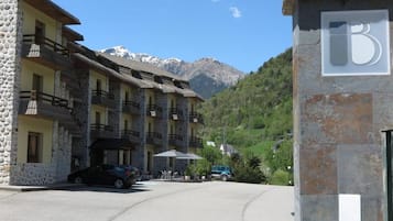 A hotel with stone facade, multiple balconies, and a mountain backdrop.