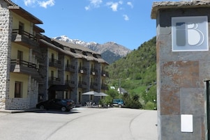 Un hotel de fachada de piedra, con varios balcones y el paisaje de una montaña al fondo.