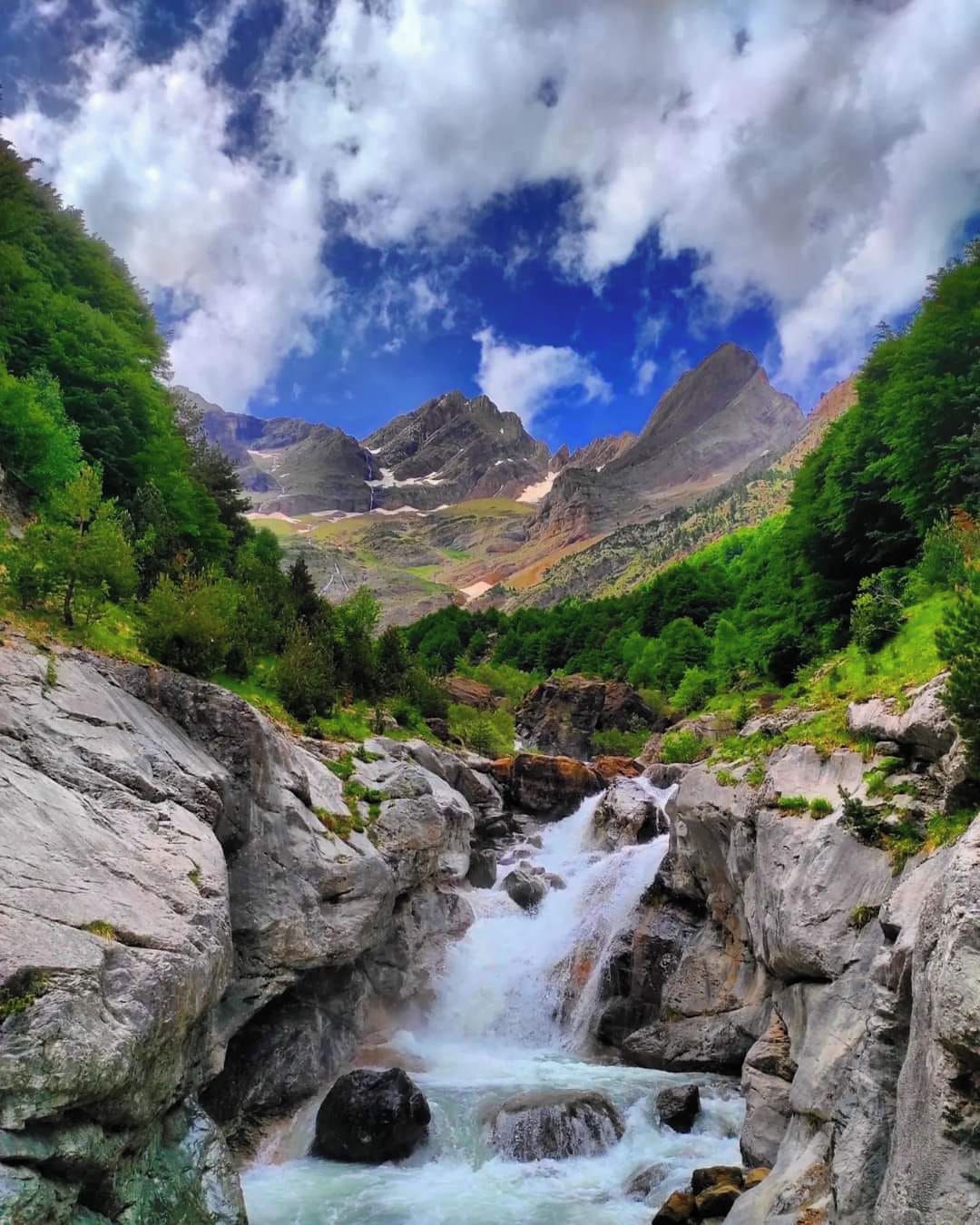 Un paisaje montañoso con cascada, terreno rocoso y abundante vegetación.