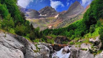 Un paisaje montañoso con cascada, terreno rocoso y abundante vegetación.