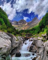 Un paisaje montañoso con cascada, terreno rocoso y abundante vegetación.