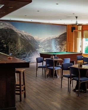 A pool table in a room with a mountain view mural, wooden flooring, and blue chairs. - Snö Bielsa (Bielsa)