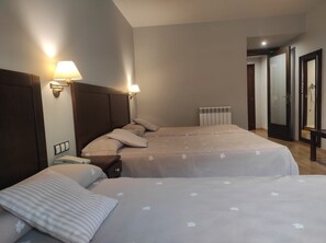 Quarto de hotel com duas camas, uma mesa de cabeceira, um abajur, um radiador e um espelho.
