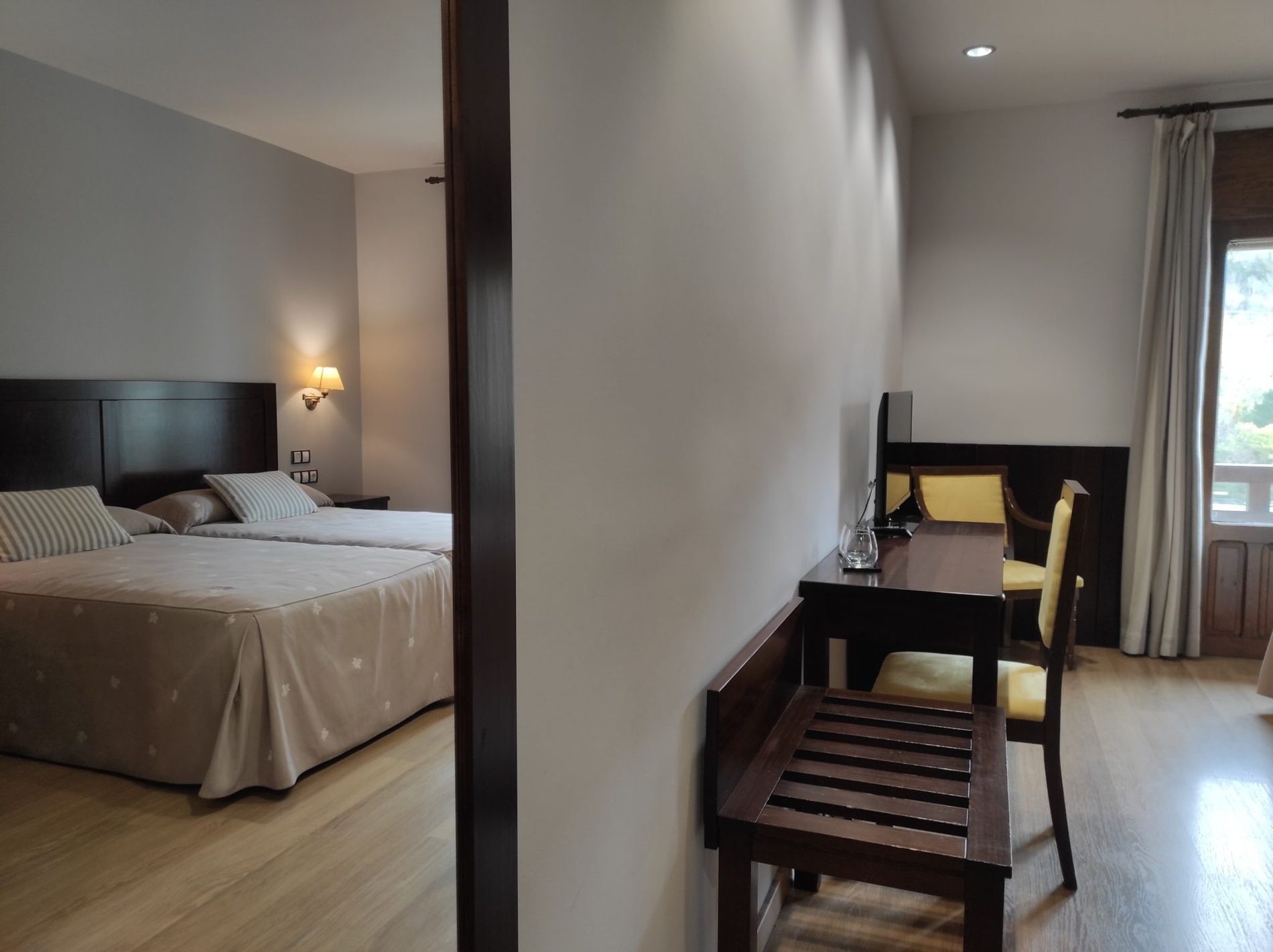 A hotel room with a bed, bedside table, lamp, and a desk with a chair.