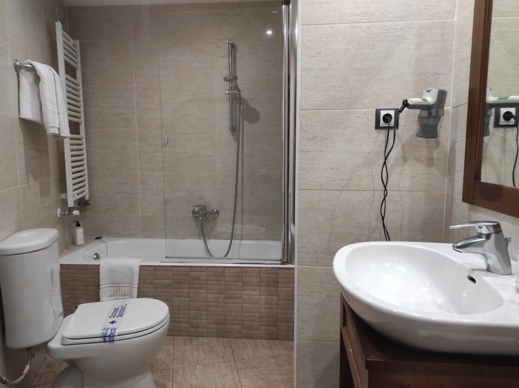 Un baño moderno con ducha de vidrio, inodoro blanco y lavamanos con espejo.