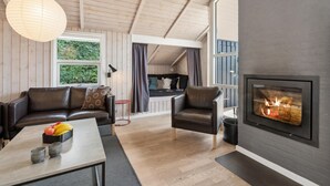 A cozy living room with a fireplace, leather sofas, a dining table with fruit, and a view of the outdoors. - 3 bedroom nice home in Broager (Broager)