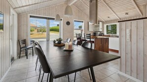 A spacious dining area with a large table and chairs, a kitchen in the background, and a view of the outdoors. - 3 bedroom nice home in Broager (Broager)