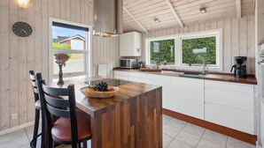 A modern kitchen with wooden walls, a central island, white cabinets, and a view of greenery outside. - 3 bedroom nice home in Broager (Broager)