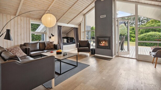 A cozy living room with a fireplace, wooden floors, and large windows offering a view of the outdoors. - 3 bedroom nice home in Broager (Broager)