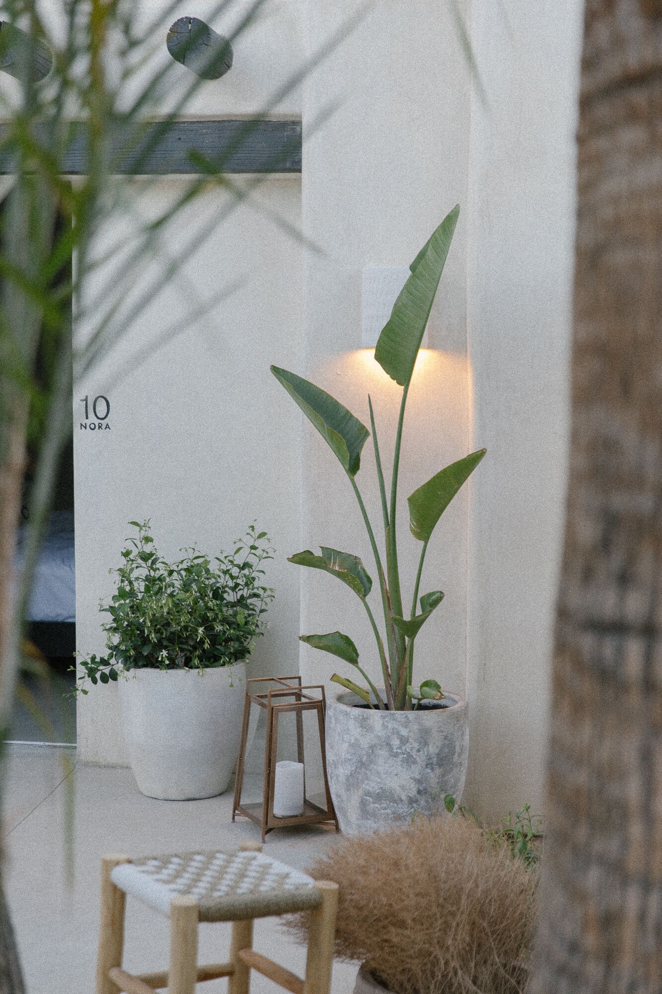 Un rincón al aire libre pequeño y acogedor con una silla de madera y una mesa pequeña, rodeado de plantas en macetas y una jardinera de piedra.