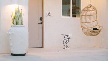 A modern building with a pool, a door labeled "Xochi Suite", a hanging chair, and a potted plant.