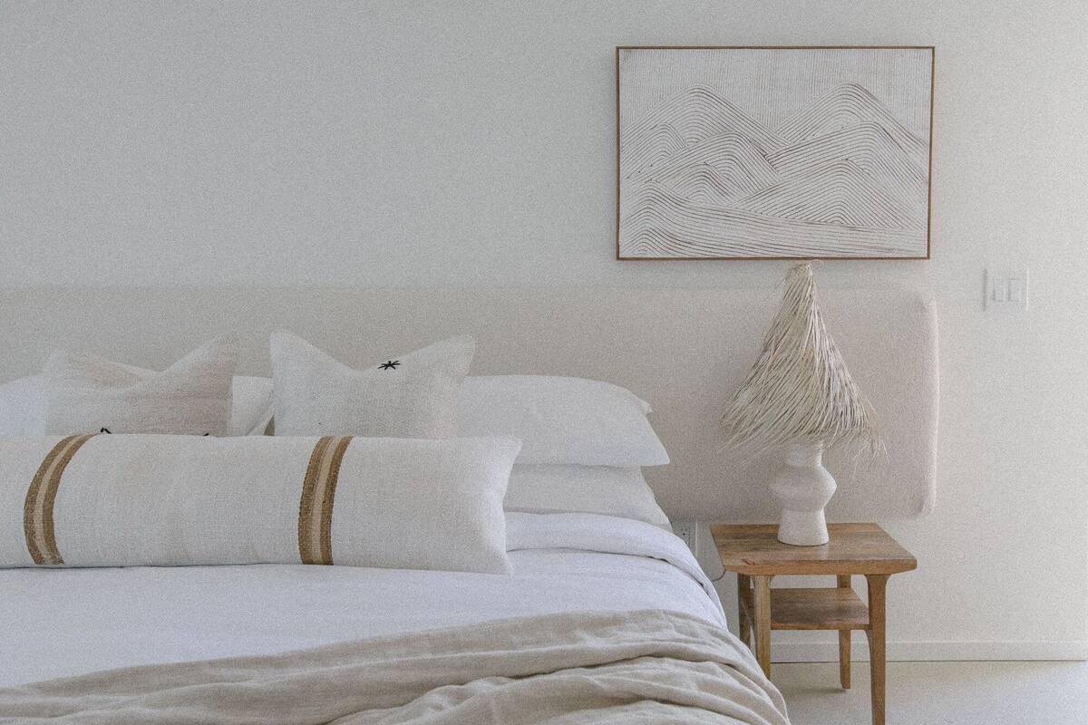 A bedroom with a bed, pillows, a bedside table with a lamp, and a framed artwork on the wall.