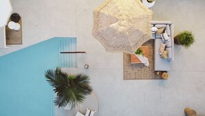 An aerial view of a pool area with a lounge chair, a small table with a plant, and a large umbrella. - Yara Hotel (Palm Springs)