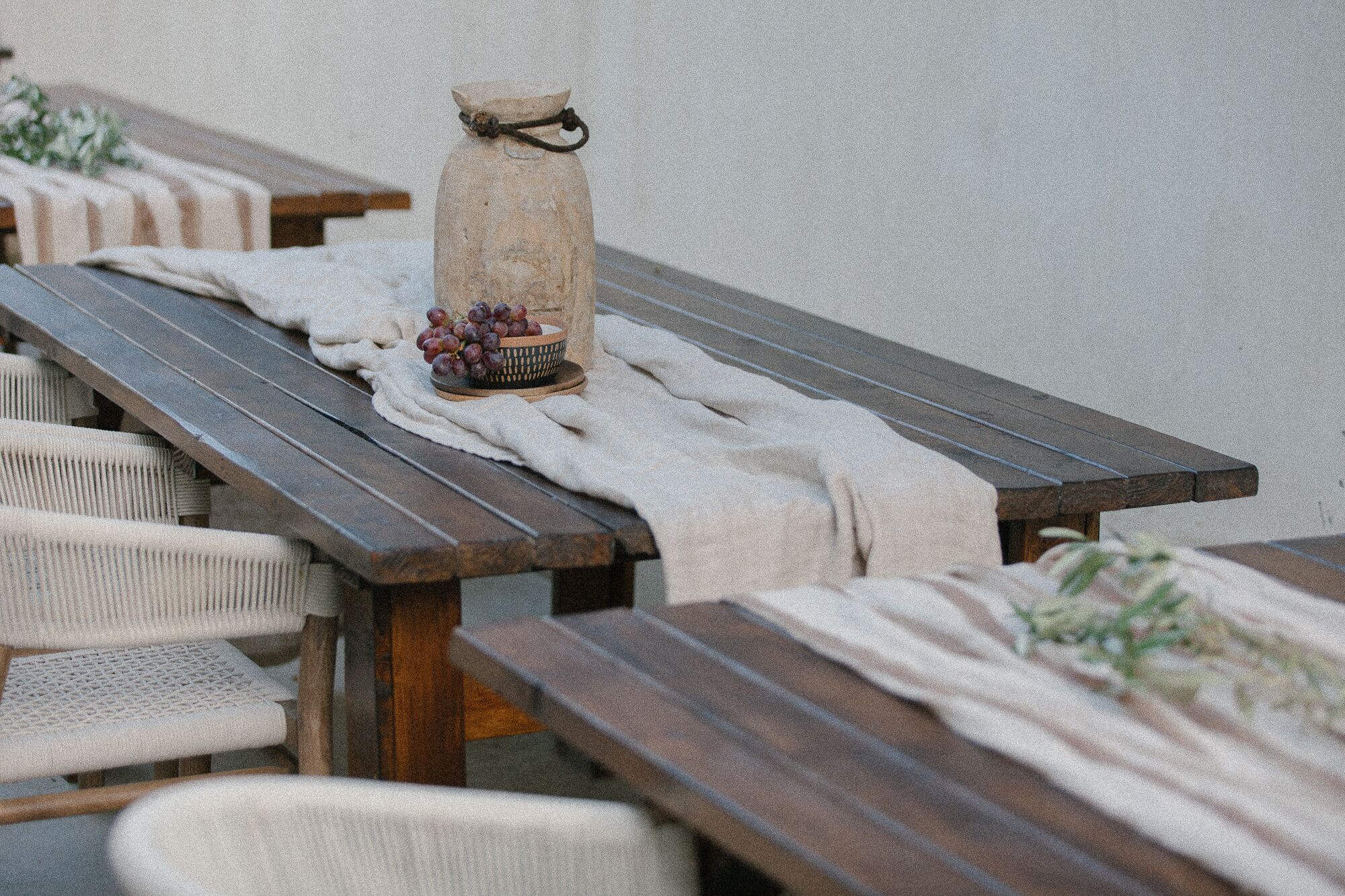 A rustic outdoor dining area with wooden benches and a stone jug with grapes.