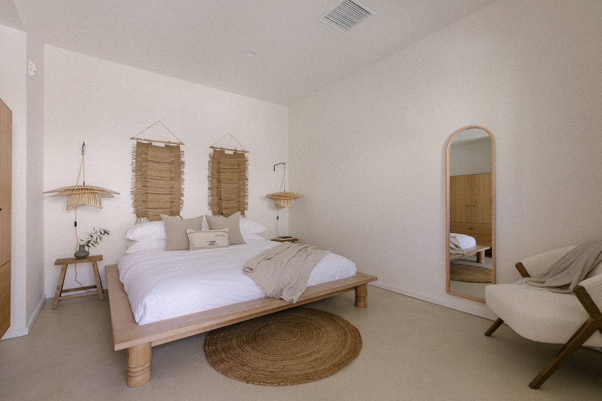 A bedroom with a wooden bed, a round woven rug, a chair, and two wall-mounted lamps.
