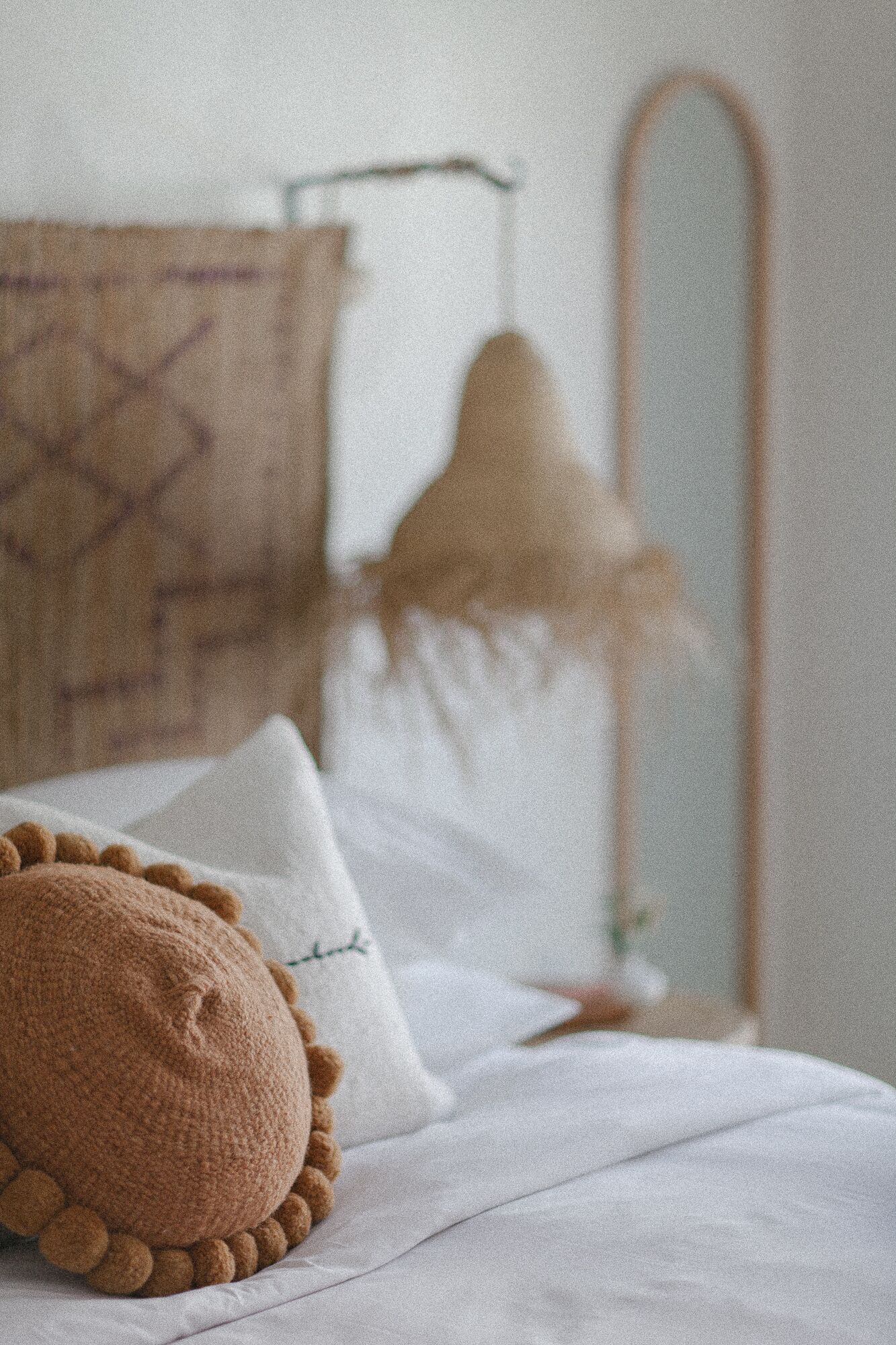 Un letto con un cuscino lavorato a maglia marrone e un cuscino bianco con ricami, una struttura letto in metallo e uno specchio fissato alla parete.