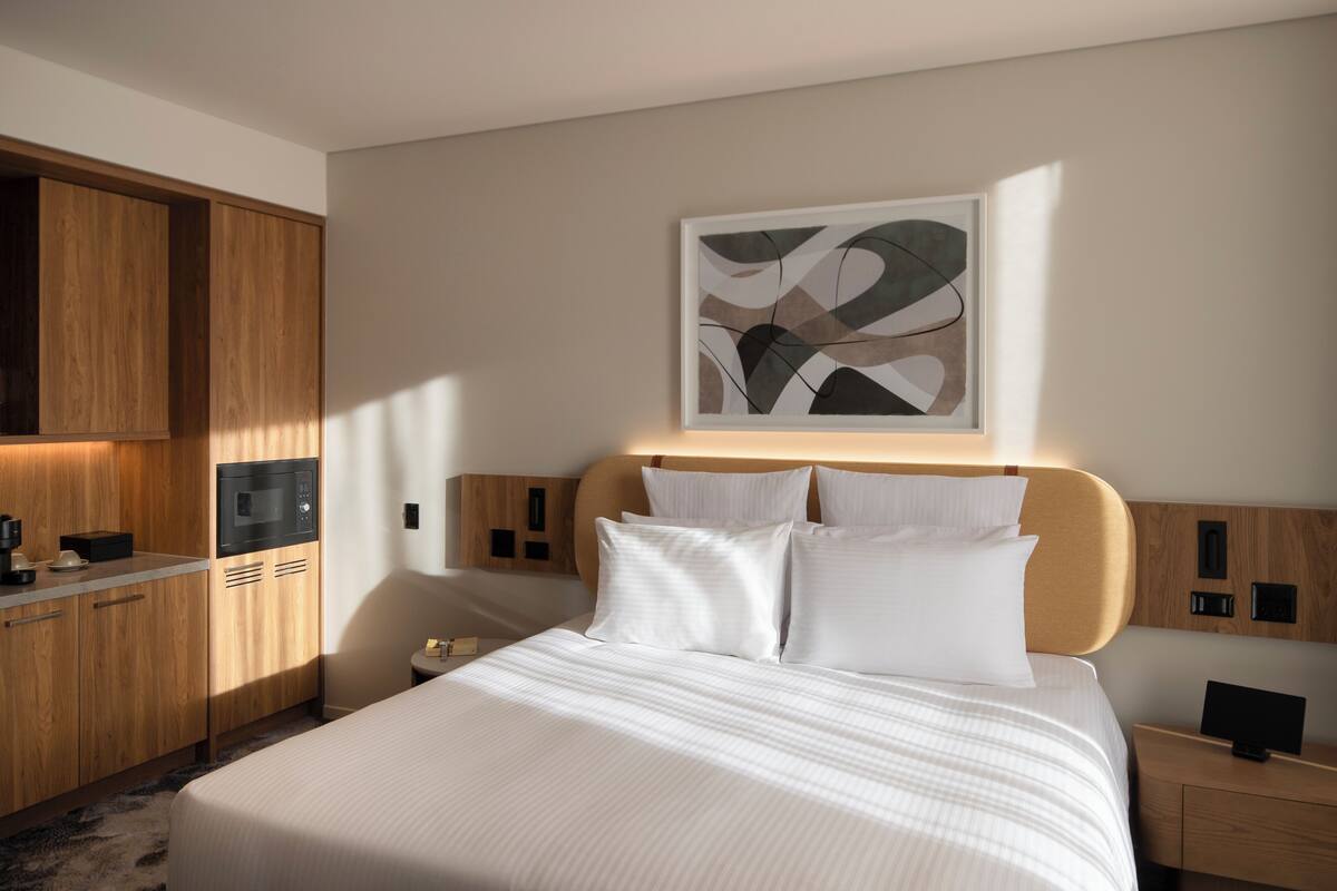 A modern hotel room with a large bed, wooden cabinetry, a microwave, and a wall-mounted artwork.