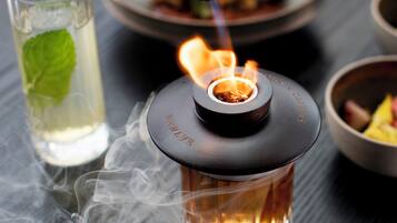 A close-up of a glass container with a lit burner, surrounded by smoke.