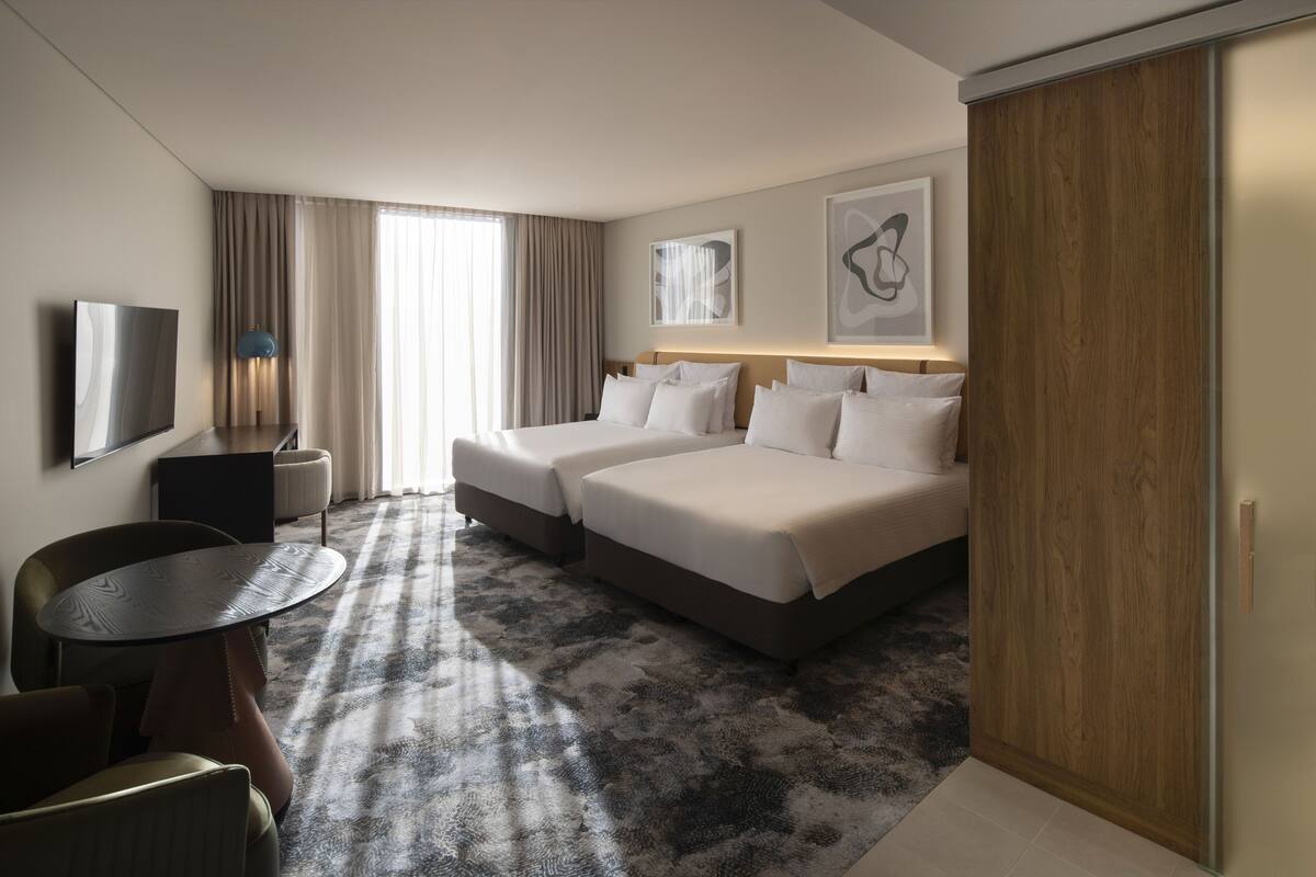 A hotel room with two beds, a TV, a desk, and a chair.