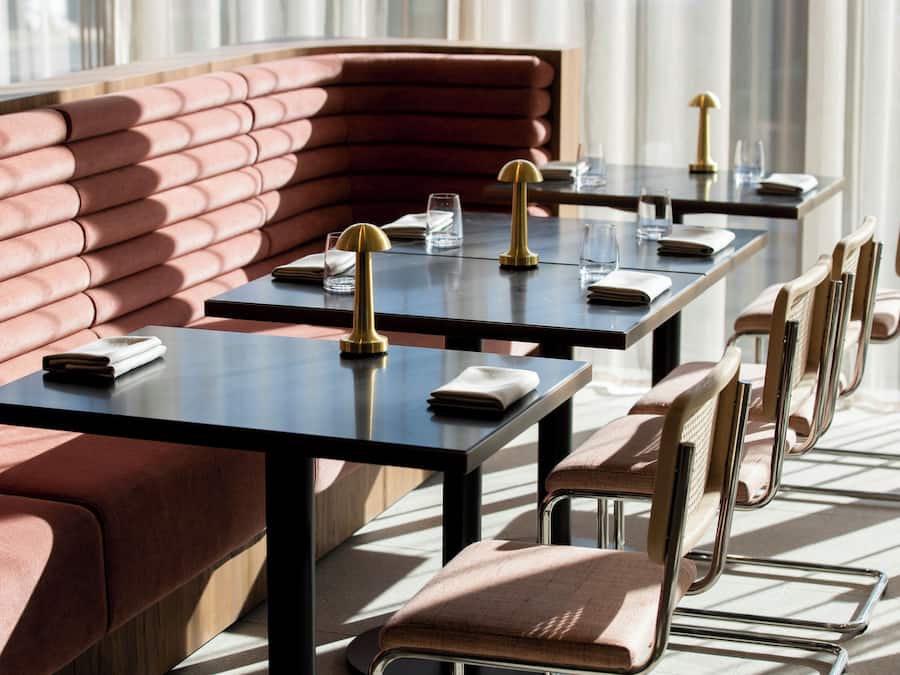 Tyylikäs, moderni ravintola, jossa on pehmustetut istuimet, mustat pöydät ja kultaiset yksityiskohdat.