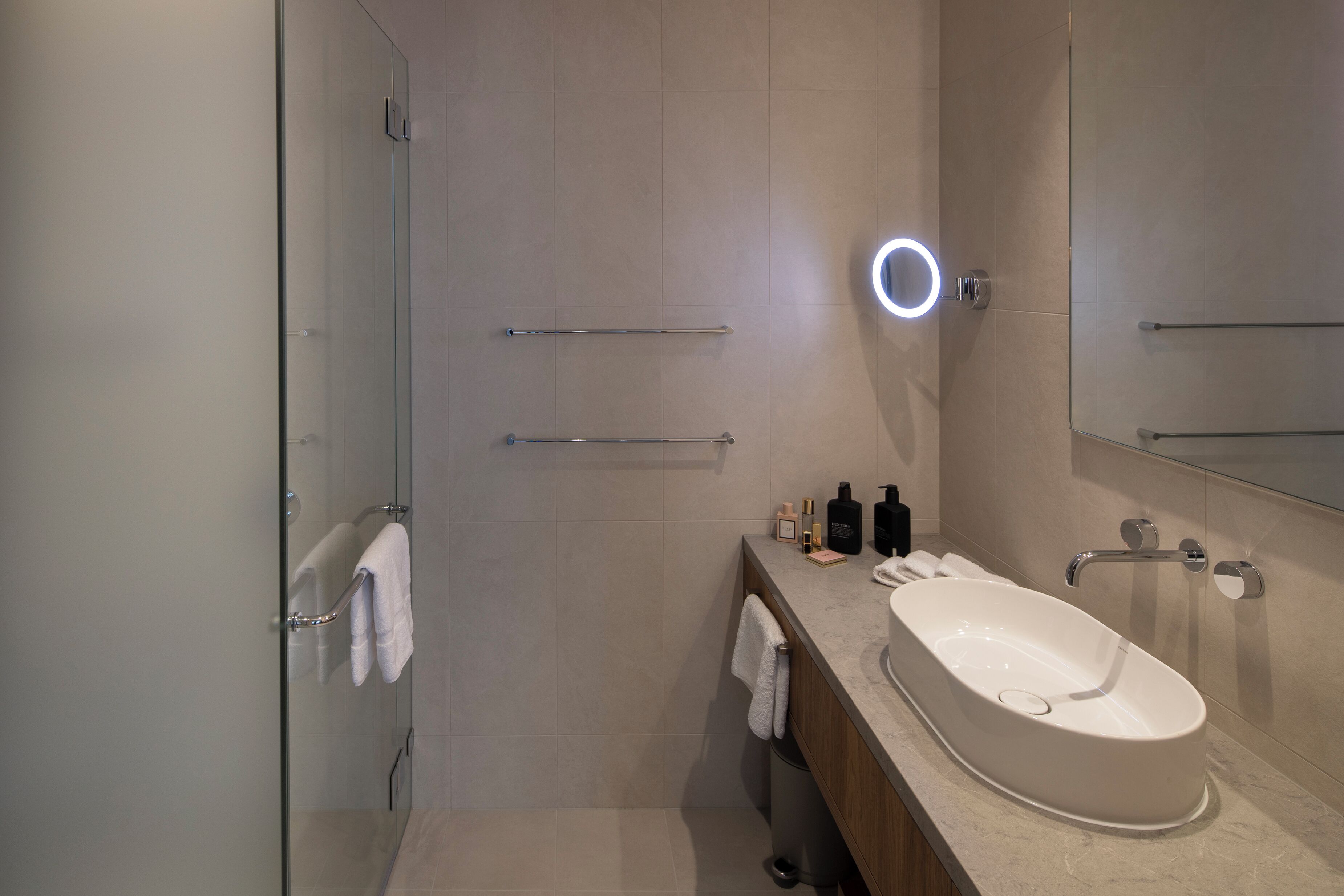 Een moderne badkamer met een glazen douchecabine, een groot ovaal wastafel en een spiegel met ingebouwde verlichting.