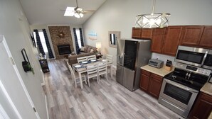 Eine moderne Küche mit Edelstahlgeräten, ein Essbereich mit weißen Stühlen und ein Wohnzimmer mit Kamin.