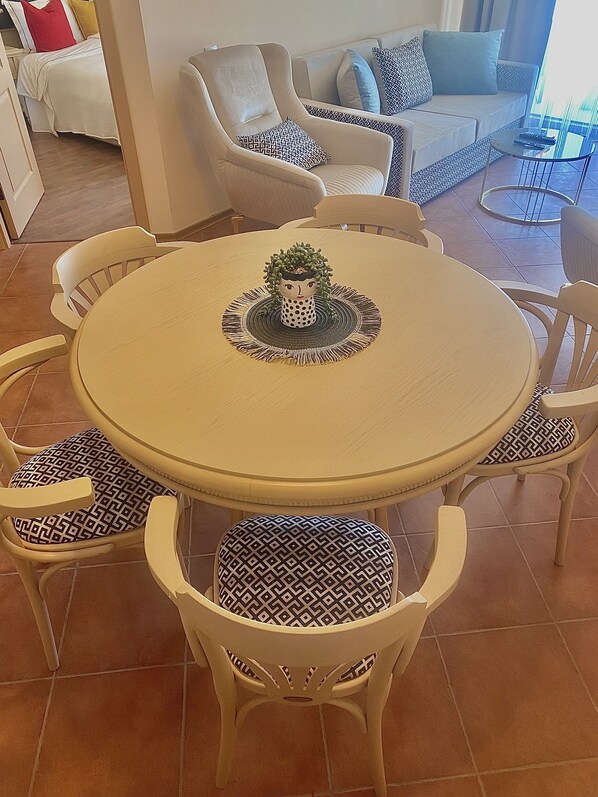 Uma mesa de jantar redonda com seis cadeiras, cada uma com almofadas estampadas, em volta de um chão ladrilhado.