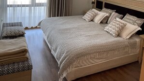 Une chambre à coucher avec un grand lit, une table de chevet, un banc et une fenêtre avec des rideaux.