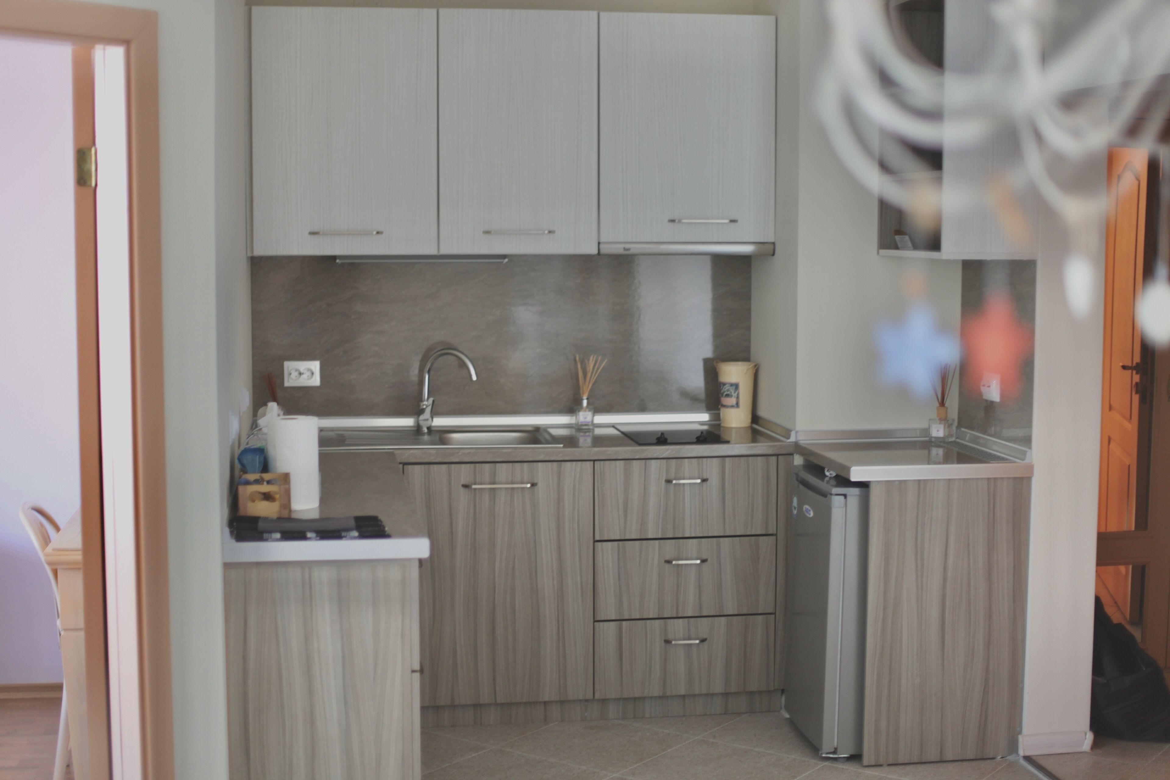 A modern kitchen with light wood cabinets, a stainless steel sink, and a compact dishwasher.